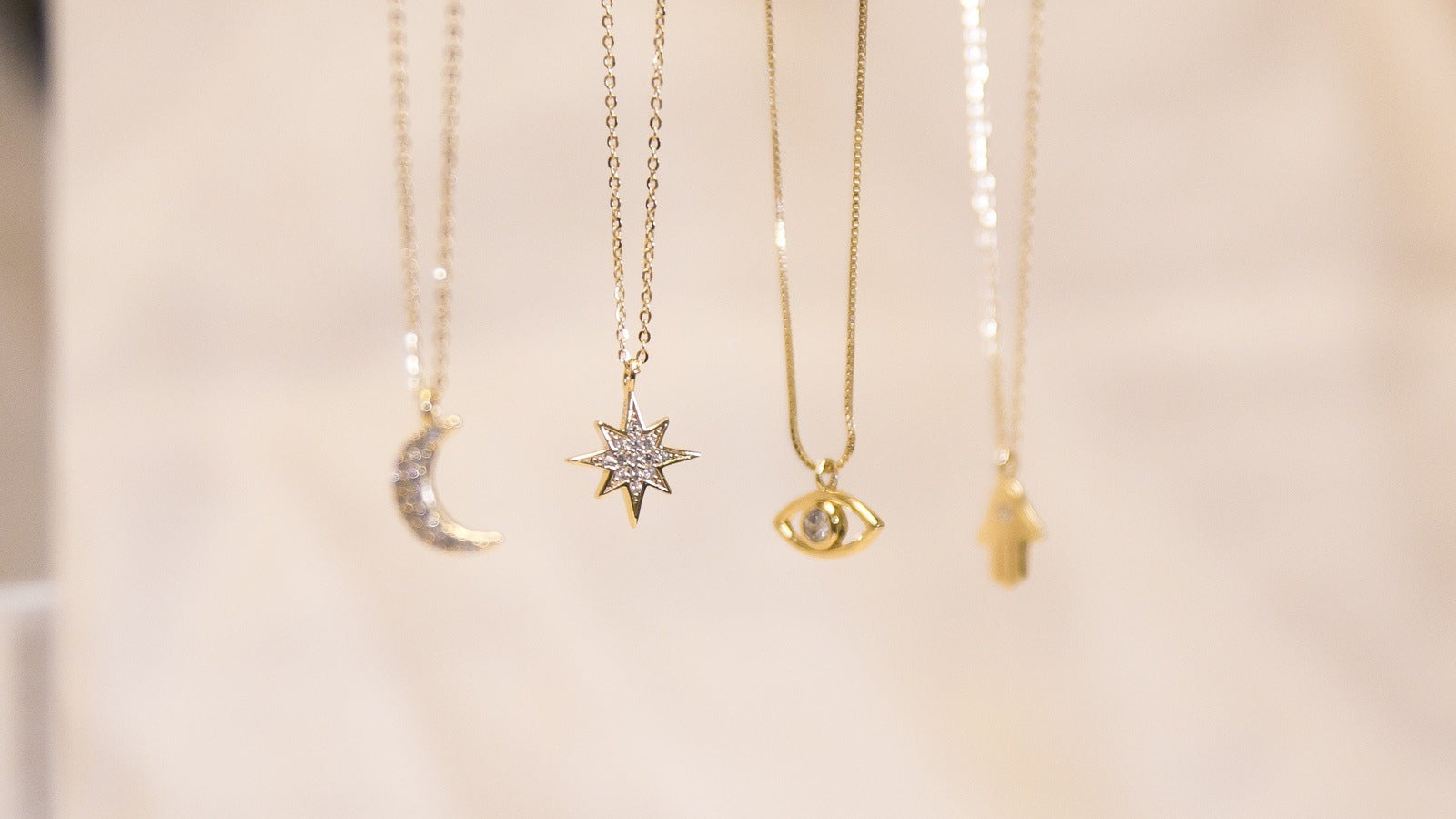 four sterling silver and 14k gold pendant necklaces. A crescent moon pendant, starburst pendant, evil eye pendant, and hamsa pendant are visible
